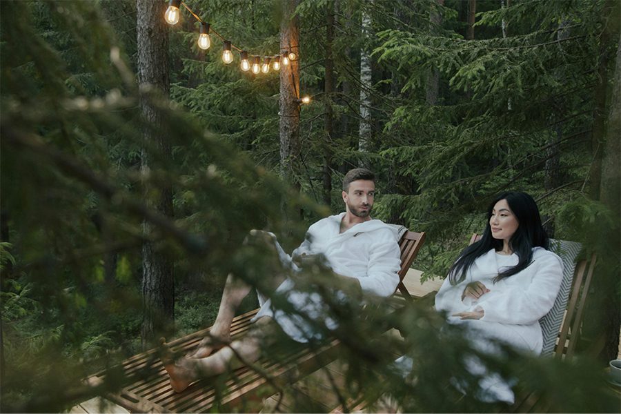 A couple wearing bathrobes and relaxing on reclining chairs in a forest